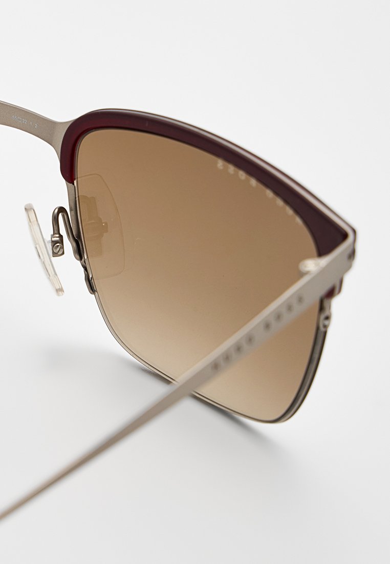 Sonnenbrille mit braunen Verlaufslinsen, silbernem Metallrahmen und bordeauxroten Kunststoffakzenten an der Oberseite. Inklusive Nasenpolster und dünnen Bügeln.