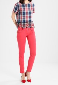 Top de cuadros de manga corta con un dobladillo de flecos, combinado con unos pantalones ajustados rosa brillante y tacones de aguja rojos. Texturas suaves y colores vibrantes.