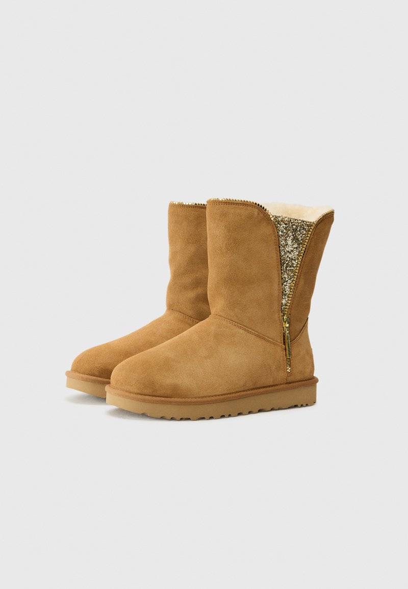 Beige Wildleder-Stiefeletten mit einem weichen, weißen Fellfutter und einem seitlichen Reißverschluss in Gold. Die Sohle ist flach und hat ein strukturiertes Grip-Muster.