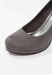 Chaussure à talon haut en daim gris avec un bout rond et un dessus ouvert, présentant une semelle intérieure métallique lisse et une surface extérieure texturée.