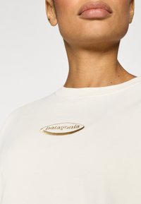 Λευκό βαμβακερό t-shirt με στρογγυλή λαιμόκοψη, διακοσμημένο με κεντημένο μεταλλικό χρυσό λογότυπο "Patagonia" στο στήθος. Απαλή υφή.