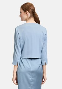 Jasnoniebieski krótki top z rękawami do trzech czwartek. Charakteryzuje się gładką fakturą, delikatnymi rozporkami na końcach rękawów oraz prostym dekoltem.