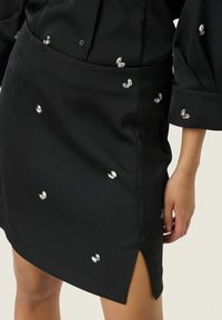 Jupe noire avec un design ajusté, dotée d'une fente latérale et ornée de petites accents réfléchissants uniformément répartis sur le tissu.