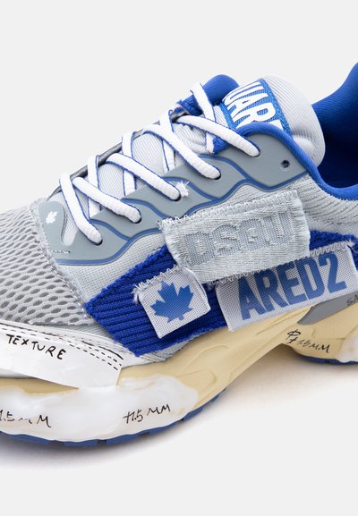 Baskets grises et bleues avec des lacets blancs, tissu en maille, patchs cousus montrant une feuille d'érable et le texte "DSQUARED2".