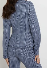 Sako s námořnickým a bílým kostkovaným vzorem, přiléhavý střih s dlouhými rukávy, manžetami na knoflíky a peplum detaily na zadní straně.