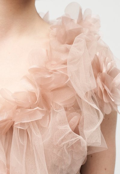 Haut en tulle rose clair avec des appliqués floraux et des couches transparentes, créant un effet texturé et superposé avec des détails doux et fluides.
