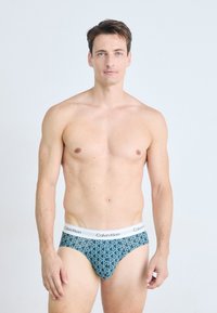 Kék mintás boxer alsónadrág geometrikus mintával, puha anyagból, fehér rugalmas derékkal, rajta a "Calvin Klein" logóval.