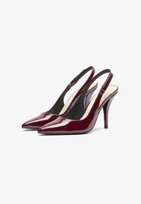 Decolté slingback in vernice bordeaux con punta a forma di punta e tacco a stiletto di 10 cm. Presenta un design con ritagli e una cintura alla caviglia regolabile.