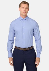 Camicia a quadri blu chiaro con maniche lunghe, colletto button-down e bottoni bianchi, abbinata a pantaloni scuri e una cintura marrone.