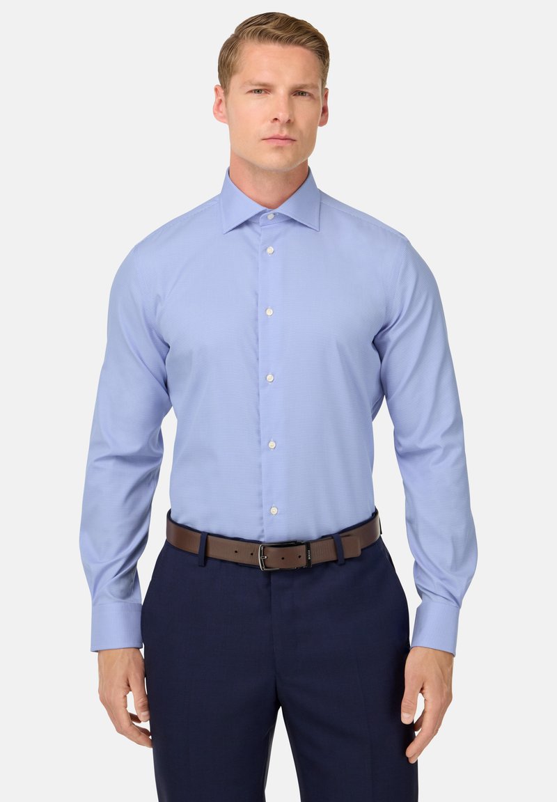 Camicia a quadri blu chiaro con maniche lunghe, colletto button-down e bottoni bianchi, abbinata a pantaloni scuri e una cintura marrone.