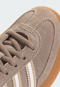 Baskets en daim marron avec deux rayures en zigzag blanches, surface texturée, design à lacets et semelle en caoutchouc gomme.