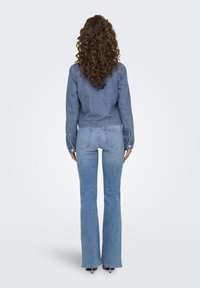 Veste en denim à manches longues et taille cintrée, associée à un jean clair évasé. Les deux présentent une texture douce et une teinte bleue classique.