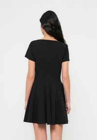 Μαύρο φόρεμα με κοντά μανίκια και φουσκωτή φούστα, με διακριτικό στρογγυλό λαιμό και φερμουάρ στο πίσω μέρος. Με λεία υφή και εφαρμοστή ζώνη στη μέση.