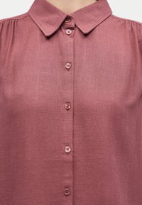 Πουκάμισο με κουμπιά σε απαλό μοβ χρώμα, με μυτερό γιακά και ορατή υφή υφάσματος, κομμένο στο ύψος του λαιμού και του πάνω μέρους του κορμού.