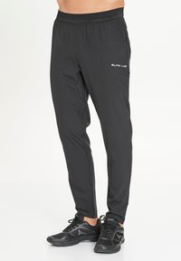 Schwarze Sporthose mit tailliertem Design, ausgestattet mit einem Kordelzugbund und Logodetail am linken Oberschenkel. Hergestellt aus leichtem Material.