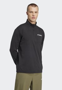 Black mid-layer pullover with a quarter zip, featuring a chest pocket and white "Terrex" logo. Long sleeves, soft fabric, and relaxed fit.