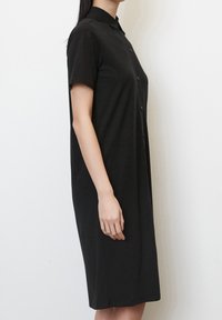 Svart skjortklänning med korta ärmar, enkel krage, knäd length, tillverkad av mjukt tyg, slät textur och rak siluett.