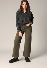 Zwarte blouse met patroon en kraag, olijfgroene wijde broek en zwarte schoenen. Outfit met een relaxte pasvorm en textuurstof.