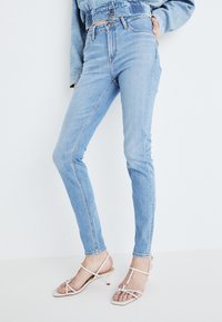 Ljust blå högmidjade jeans med smal passform, med rå nederkant och framstygn. Matchat med vita sandaler med remmar.
