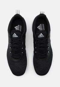 Un paio di scarpe da corsa Adidas nere con suole bianche, lacci e linguetta e soletta con marchio, viste dall'alto su uno sfondo bianco.