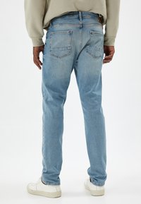 Jeans in denim azzurro chiaro con taglio dritto, dotati di due tasche posteriori e una leggera sfumatura. Indossati con una felpa grigia e sneakers bianche.