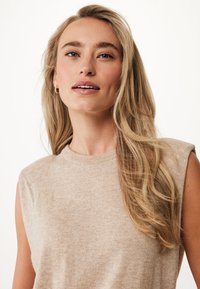 Top in maglia senza maniche color beige chiaro con scollo a girocollo, texture liscia e leggero motivo melangiato. Presenta capelli naturali che fluiscono.