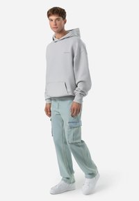 Lys grå hættetrøje med kænguru-lomme, parret med lys blå cargo bukser med sidelommer og en afslappet pasform. Hvide sneakers.