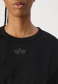 Svart bomullströja med rundad halsringning, med en subtil grå logotypdesign i mitten. Mjuk textur, korta ärmar.