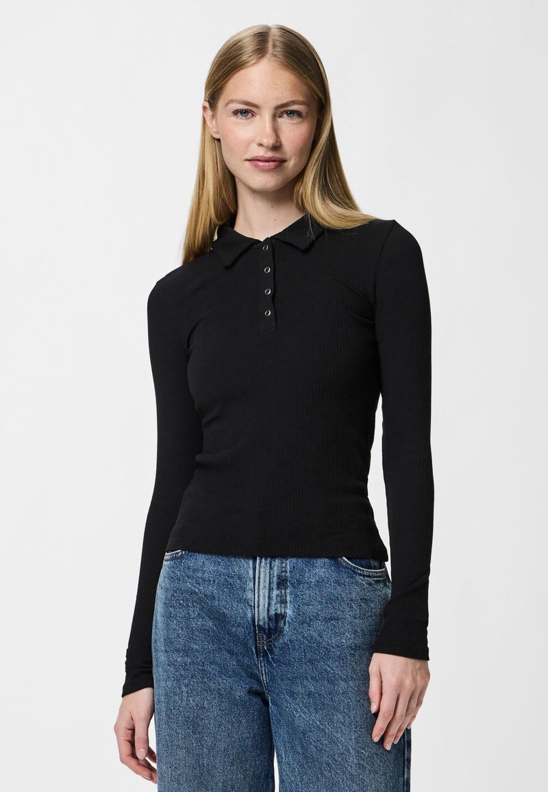 Fekete bordázott hosszú ujjú póló, gombos nyakkivágással, slim fit szabással és kerek heméssel, magas derekú kék farmernadrággal párosítva.