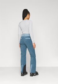 Calças de veludo cotelê azuis com uma cintura alta e painéis contrastantes nas bainhas. Textura suave com bolsos laterais e silhueta ajustada.