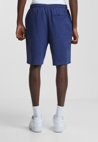 Navy blue elastic-waist shorts with a back pocket, made from soft fabric. Paired with white sneakers and ribbed white socks.