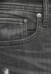Dark grey denim jeans with a slightly faded texture. Features a front pocket with a metal button and contrasting stitching.