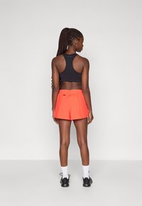 Soutien-gorge de sport noir avec un design dos nageur, associé à un short orange vif avec une taille élastique et des poches latérales.