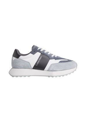 Zapatilla gris y blanca que presenta materiales de ante y cuero, con una suela texturizada, logo en el lateral y un diseño de perfil bajo.