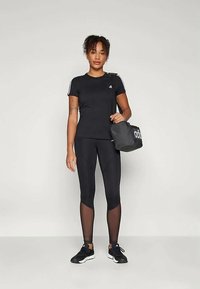 Black athletic t-shirt with short sleeves and white stripes; black leggings with sheer panels; black sports bag; athletic shoes.