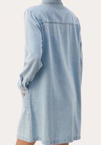 Abito in denim azzurro chiaro con maniche lunghe, collo a camicia e tasche frontali. Il tessuto è morbido, presenta una vestibilità comoda e orlo dritto.