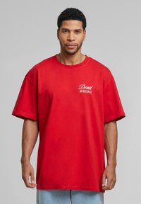 Rød oversized t-shirt lavet af bomuld, med korte ærmer og rund halsudskæring. Teksten "Dead WRONG" i hvid på brystet.