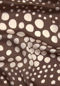 Brun stof med store, uregelmæssige hvide polka dots, der har en glat tekstur og en let glans. Designet skaber en legesyg kontrast.
