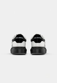Białe sneakersy z gładkiej skórzanej cholewki, czarne akcenty z lakierowanej skóry na pięcie oraz grube czarne gumowe podeszwy. Logo z tyłu.