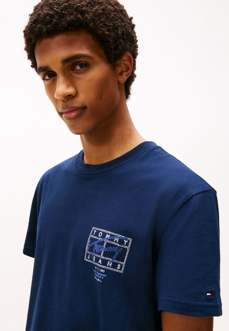 T-shirt en coton bleu marine à manches courtes, avec un logo blanc brodé sur la poitrine. Col rond côtelé et détail de logo sur la manche.