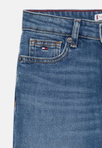 Džínsy z denimu v stredne modrom umývaní. Vlastnosti zahŕňajú prednú vrecko s malou nálepkou, medený šev a klasické zapínanie na gombík.