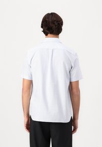 Vaaleansininen lyhythihainen kauluksellinen paita, jossa valkoiset raidat. Suora leikkaus, takana laskos ja sivuhaarat helmassa.