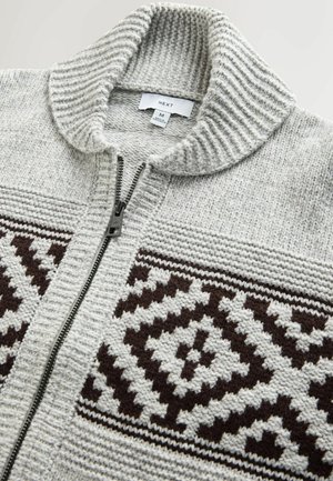 Hallitatud hall kardigan kõrge kaelusega, millel on tõmblukk ja tumepruunid mustrid rinnaosas.