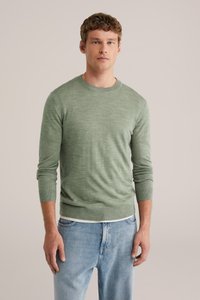 Grön crewneck-tröja i lätt material med långa ärmar och ribbade muddar. Kombinerad med ljusa denimjeans.