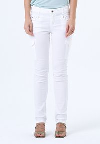 Pantalons cargo blancs extensibles avec coupe slim, dot�és de poches à patch sur les cuisses et d'un design minimaliste. Associés à des sandales vertes à brides.