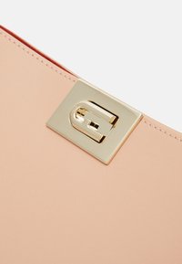 Borsa a tracolla in pelle pesca con una chiusura quadrata dorata e un logo stilizzato. Texture liscia con cuciture precise lungo i bordi.