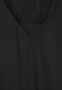 Svart tyg med V-ringning, mjuk textur och subtila sömnadsdetaljer. Tyget verkar lätt och något genomskinligt.