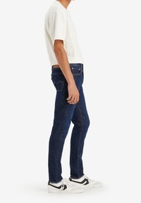 Mörkblå denimjeans med fem fickor, rak passform och subtila sömmar. Matchas med en vit T-shirt med rund halsringning och vita sneakers.