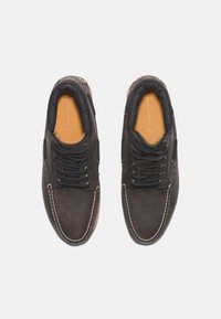 Chaussures en cuir noir à bout rond, fermeture à lacets, doublure intérieure beige et détails de coutures blanches le long de la semelle.