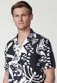 Rövidujjú ing fekete anyaggal, fehér absztrakt mintákkal, klasszikus gallérral és gombokkal az elején.